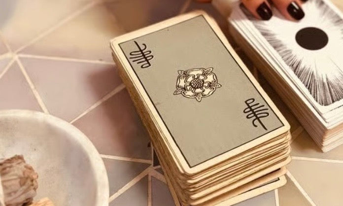 The Standard tarot cards on a geometric table, featuring intricate designs and a bowl of crystals nearby.