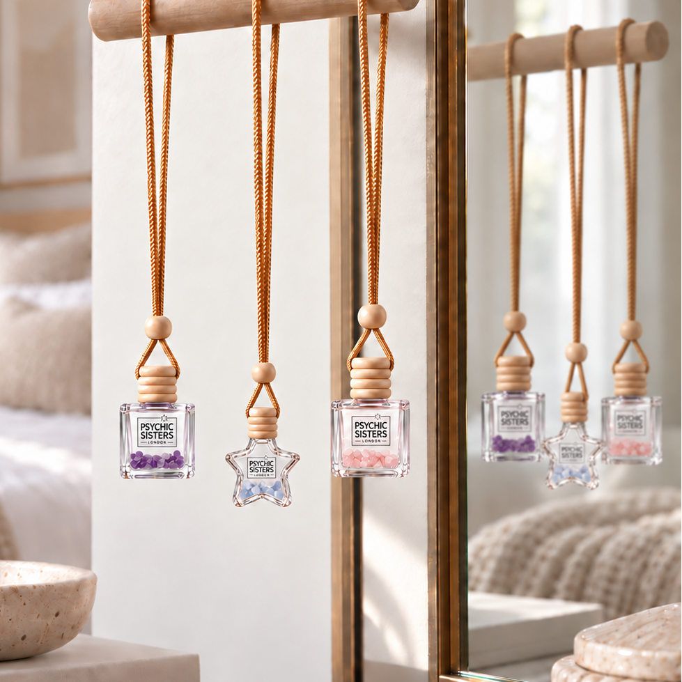 Three small clear perfume bottles with wooden atomizer tops and hanging cords are displayed on a wooden stand in a bright bedroom setting. The center bottle has a clear star-shaped cap, while the others have square clear caps with purple and pink floral details.