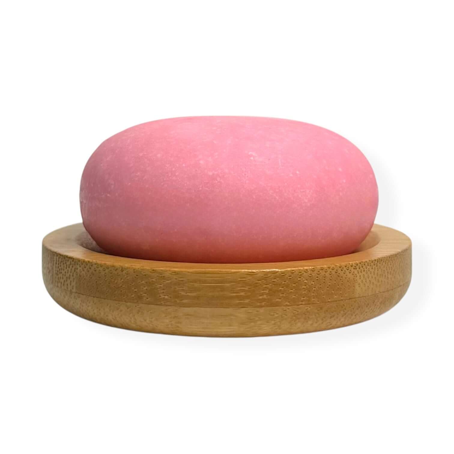 Rosemary And Biotin Shampoo Bar on a bamboo dish, featuring a vibrant pink color.