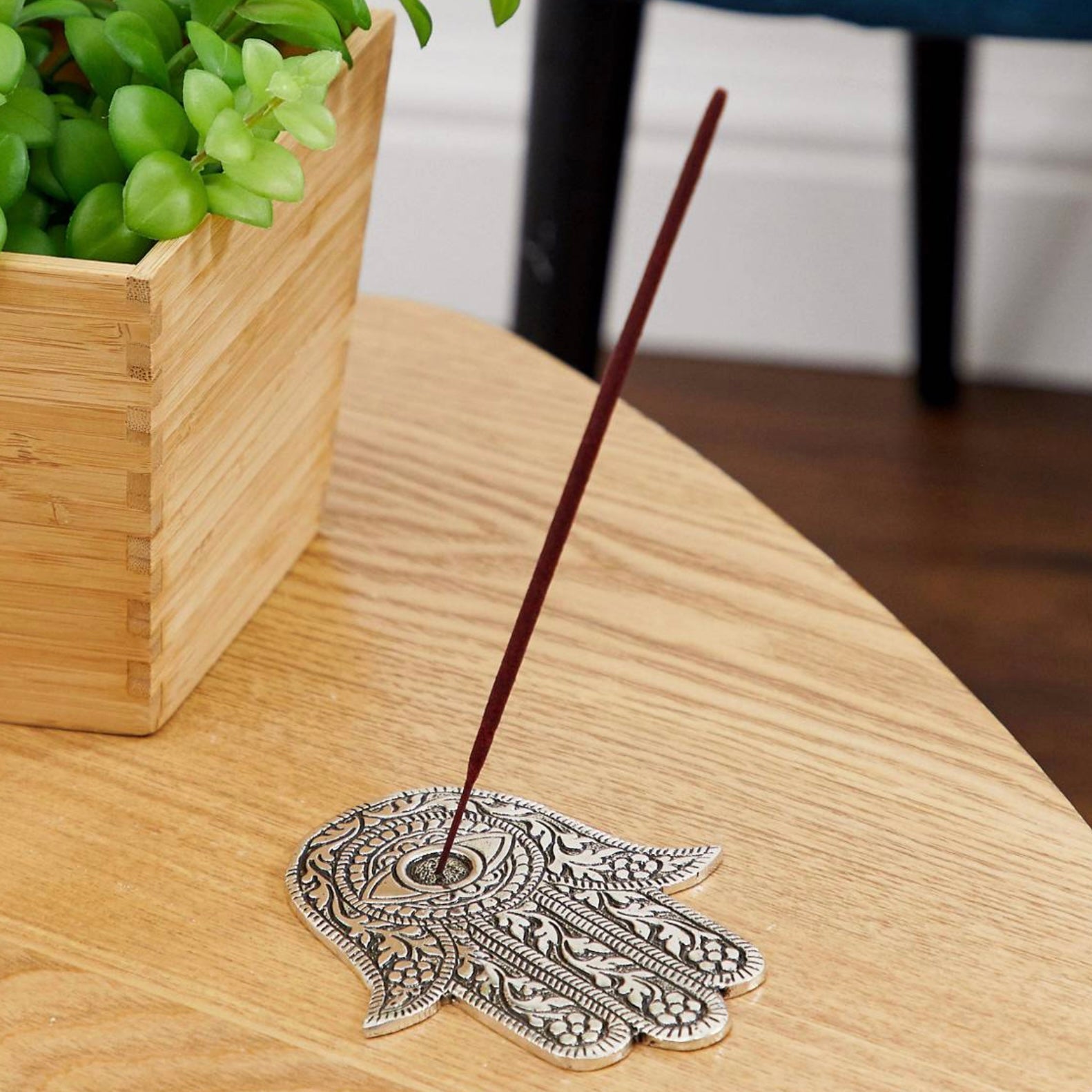 Love Incense stick holder with a Hamsa design on a wooden table, surrounded by greenery.