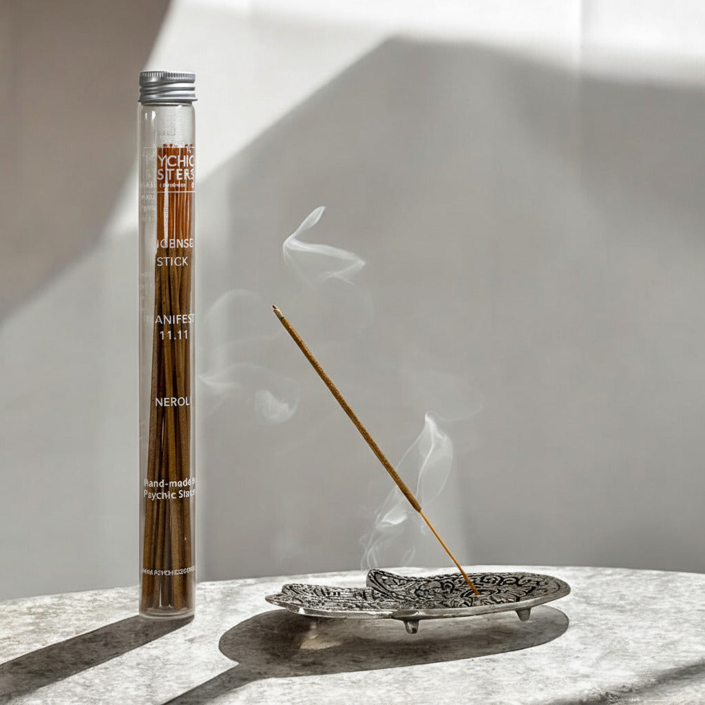 A glass tube of psychoactive incense sticks stands beside a smoking incense stick resting in a decorative metal dish on a stone surface, with dramatic shadow lighting against a neutral wall.