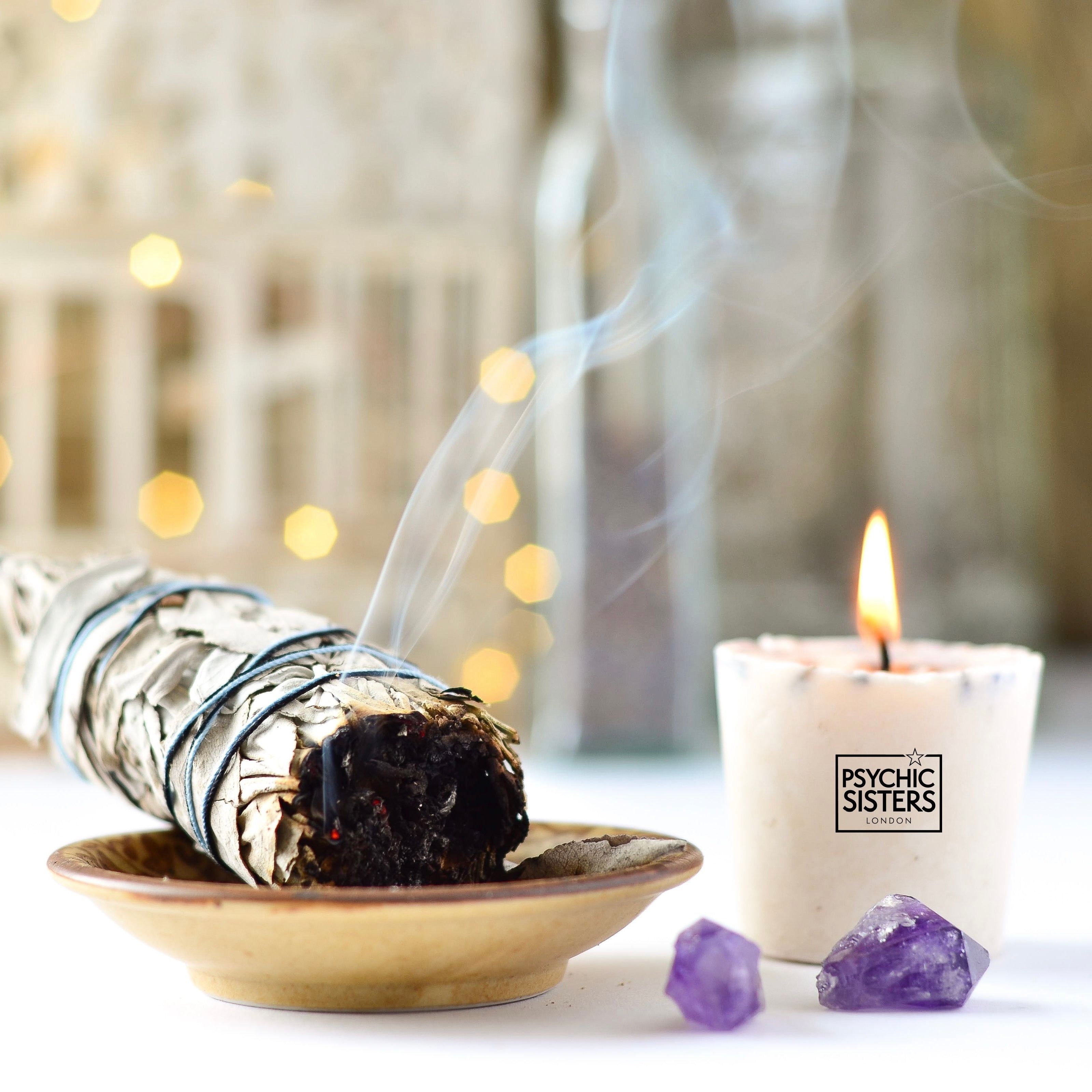 Sage sticks burning in a bowl, with a lit candle and crystals, used for cleansing negative energy.